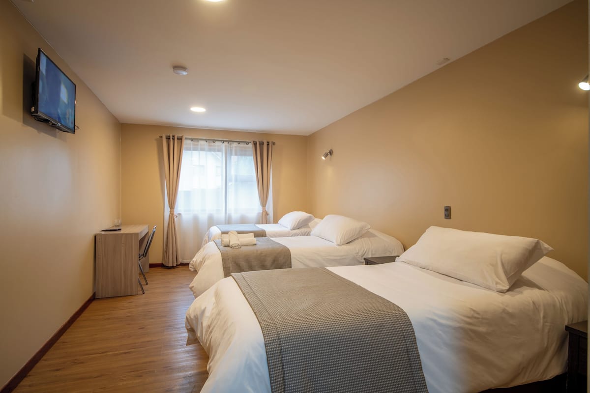 A hotel room with three beds, a desk, and a TV.
