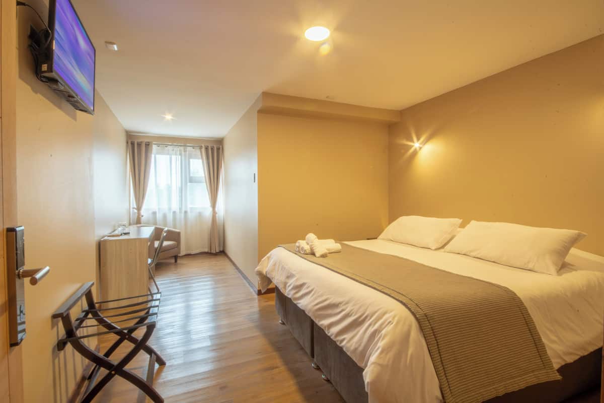 A hotel room with a bed, a desk, a chair, and a TV mounted on the wall.