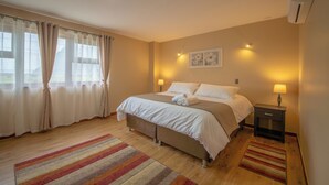 A bedroom with a bed, bedside lamps, a nightstand, a window with curtains, and a wall-mounted air conditioner. - GRAN HOTEL AYSEN (Puerto Aysen)