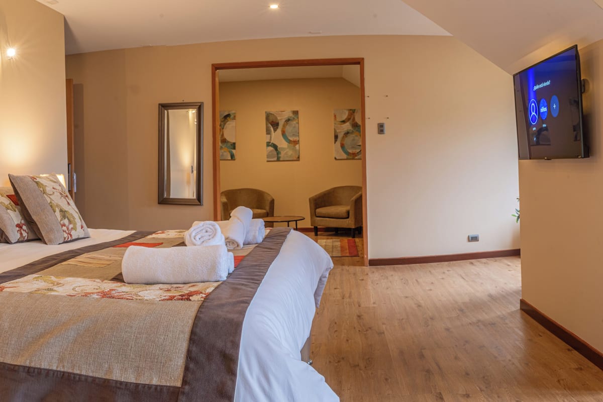 A hotel room with a large bed, a flat-screen TV mounted on the wall, and a wooden floor.