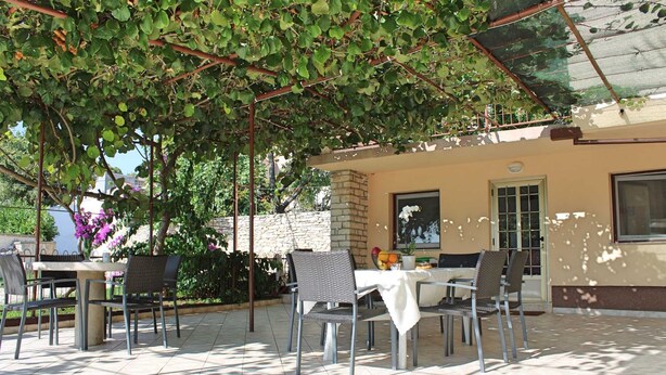 An outdoor patio with a table and chairs, surrounded by greenery and a stone wall.