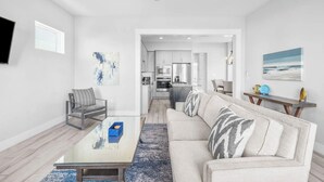 A modern living room with a sofa, coffee table, and a view into the kitchen. - 🦩Book Me Baby! Seas The Day at Inlet Beach🦩 (Inlet Beach)