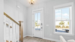 A spacious room with a wooden staircase, a white door, and a large window offering a view of the outdoors. - 🦩Book Me Baby! Seas The Day at Inlet Beach🦩 (Inlet Beach)