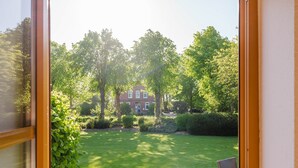 A view through a window of a well-maintained lawn, a brick house, and surrounding trees.