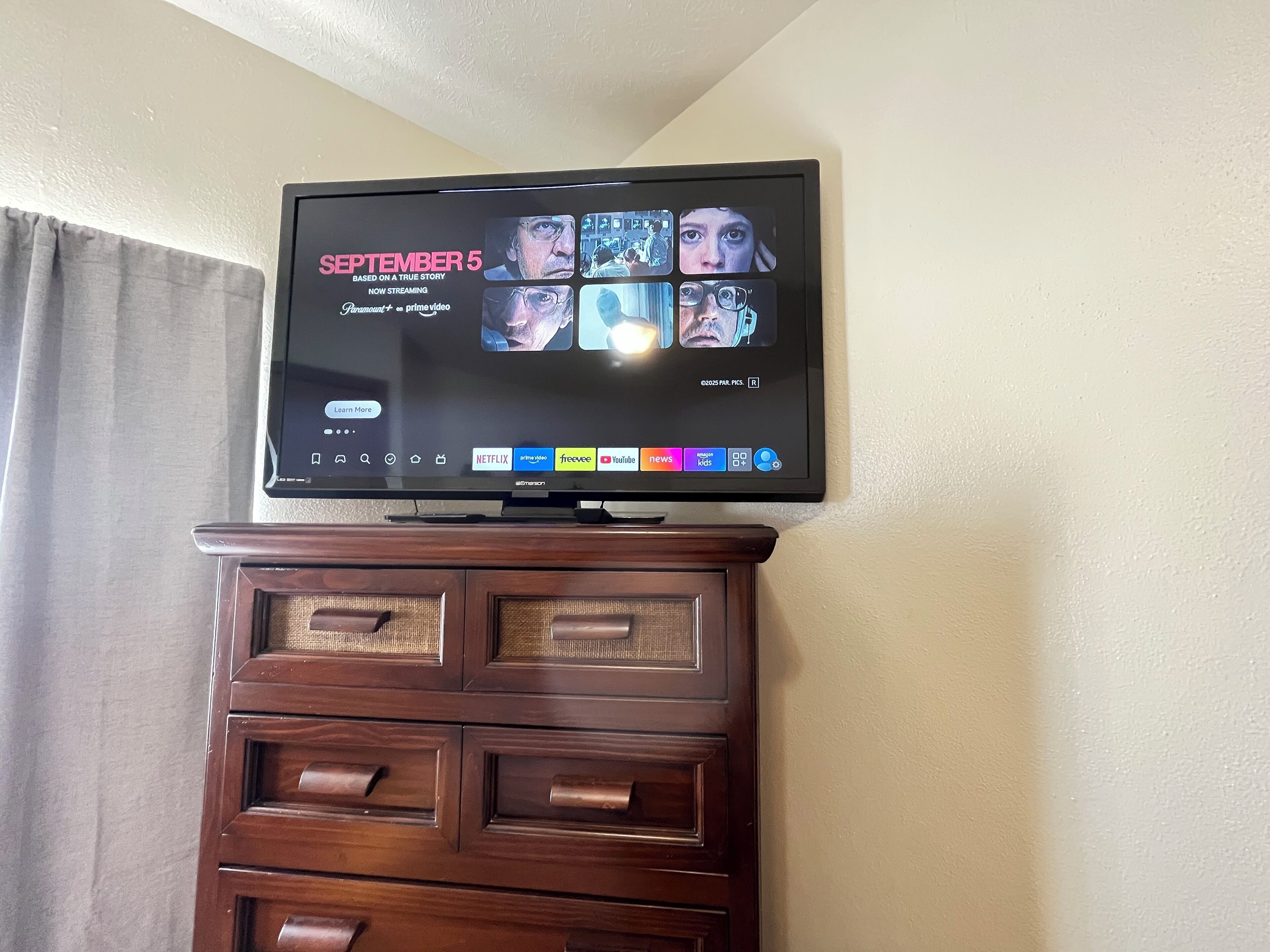 A flat-screen TV mounted on a wooden dresser with a Netflix interface displaying a movie titled "SEPTEMBER 5".