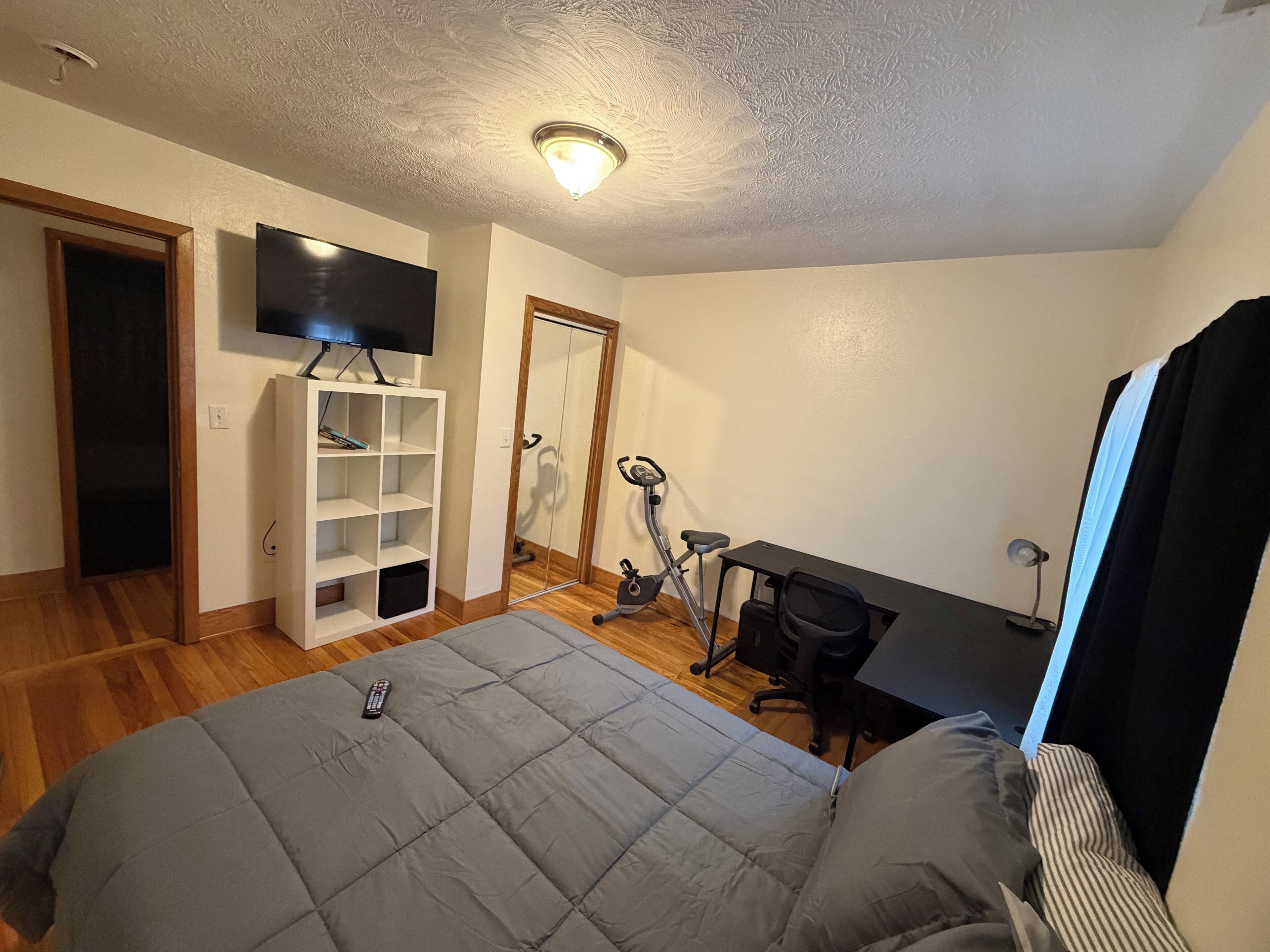 A bedroom with a bed, a TV, a desk, and an exercise bike.