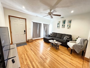 A living room with a sofa, a coffee table, a chair, a ceiling fan, and a door.