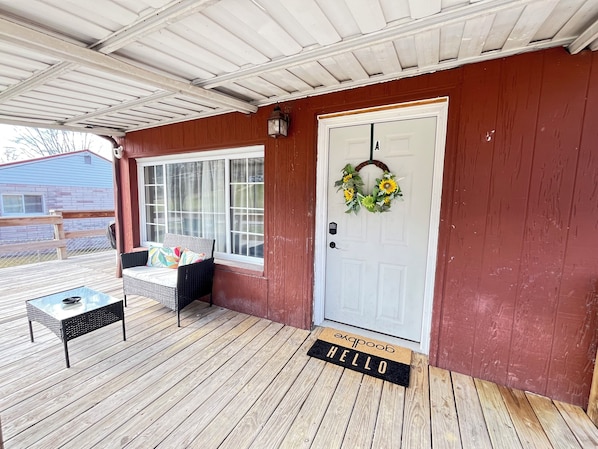 A covered porch with a white door, a bench, and a glass table.