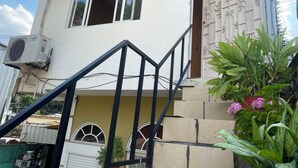 A two-story house with a staircase leading to the entrance, a security camera, and a potted plant with flowers.