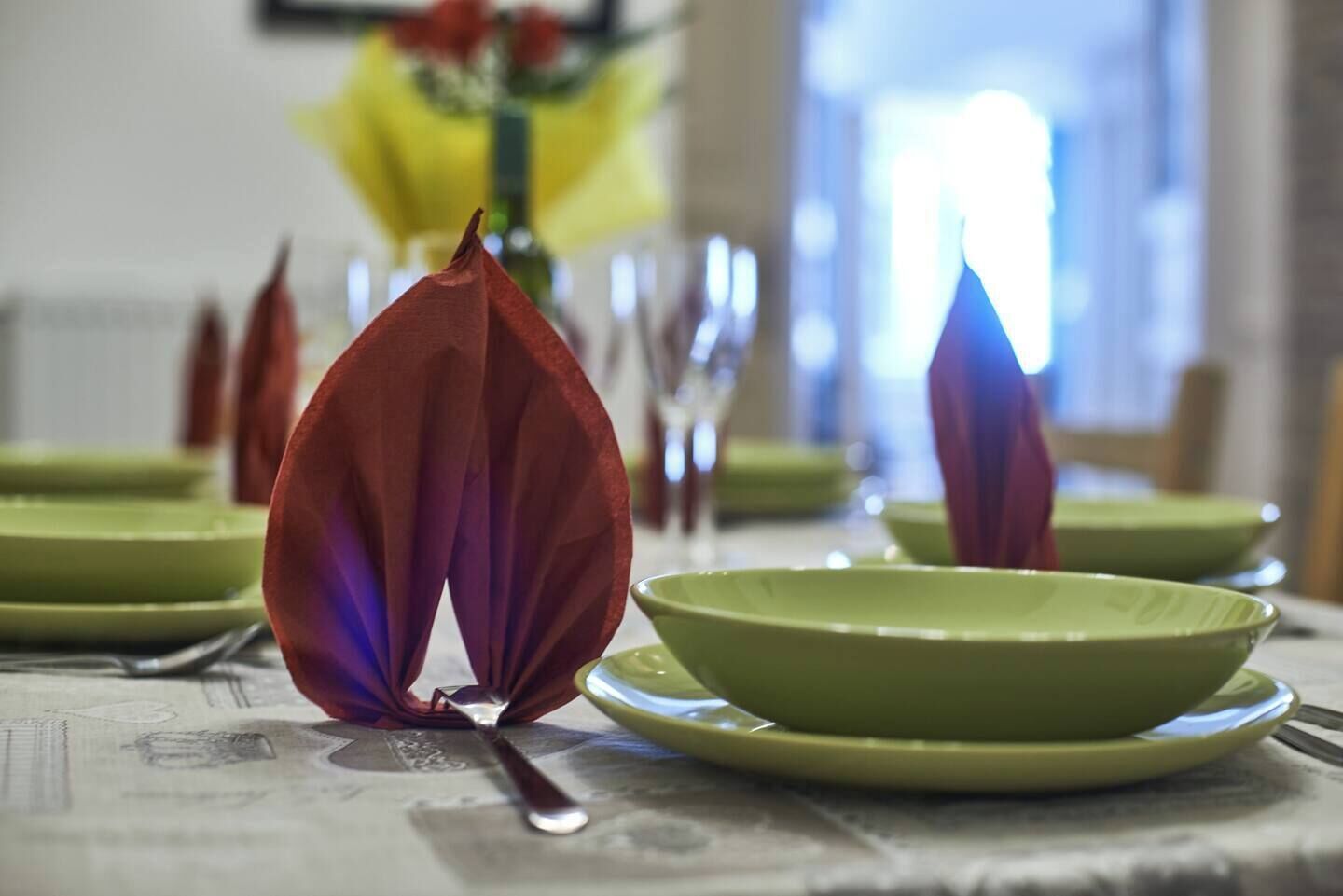 Mesa de jantar com pratos verdes e talheres, disposta com guardanapos vermelhos.