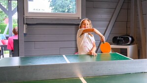 Een tafeltennistafel met net in een kamer met houten wanden en een raam.