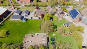 Een vogelvluchtperspectief van een woongebied met huizen, een groot groen veld en een speeltuin.