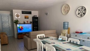 Ett vardagsrum med TV, soffa, matbord, stolar och en vattenautomat.