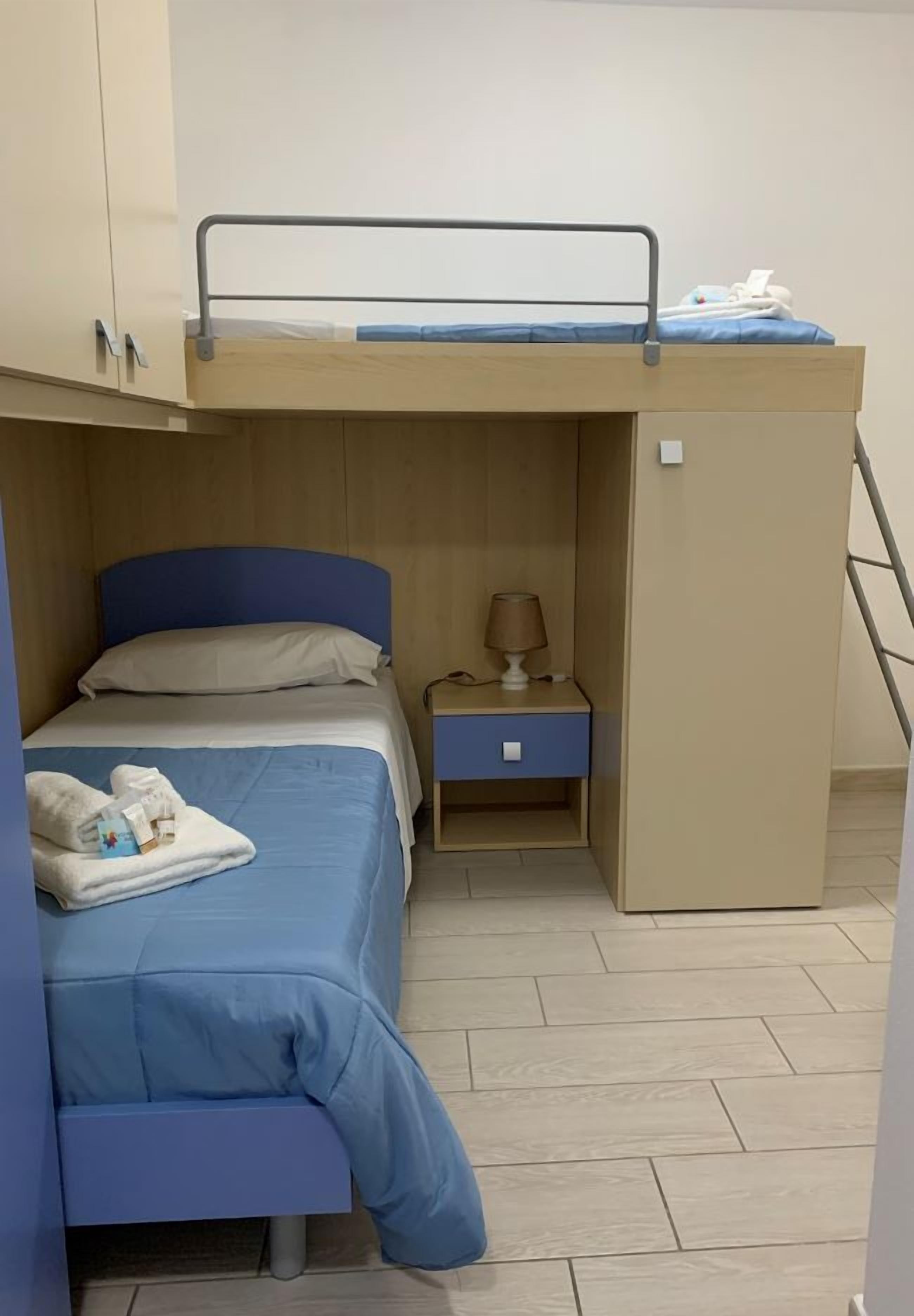 Habitación con literas, escritorio, mesita de noche, lámpara y un pequeño armario.