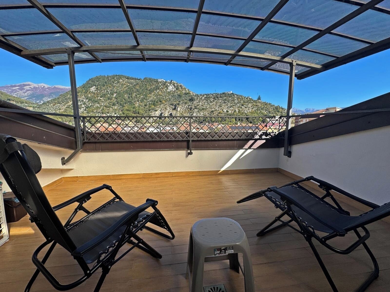 A rooftop terrace with two black lounge chairs and a small stool, overlooking a mountainous landscape.