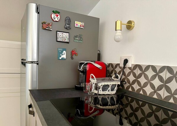 A kitchen with a refrigerator, a coffee machine, and a wall-mounted light fixture.