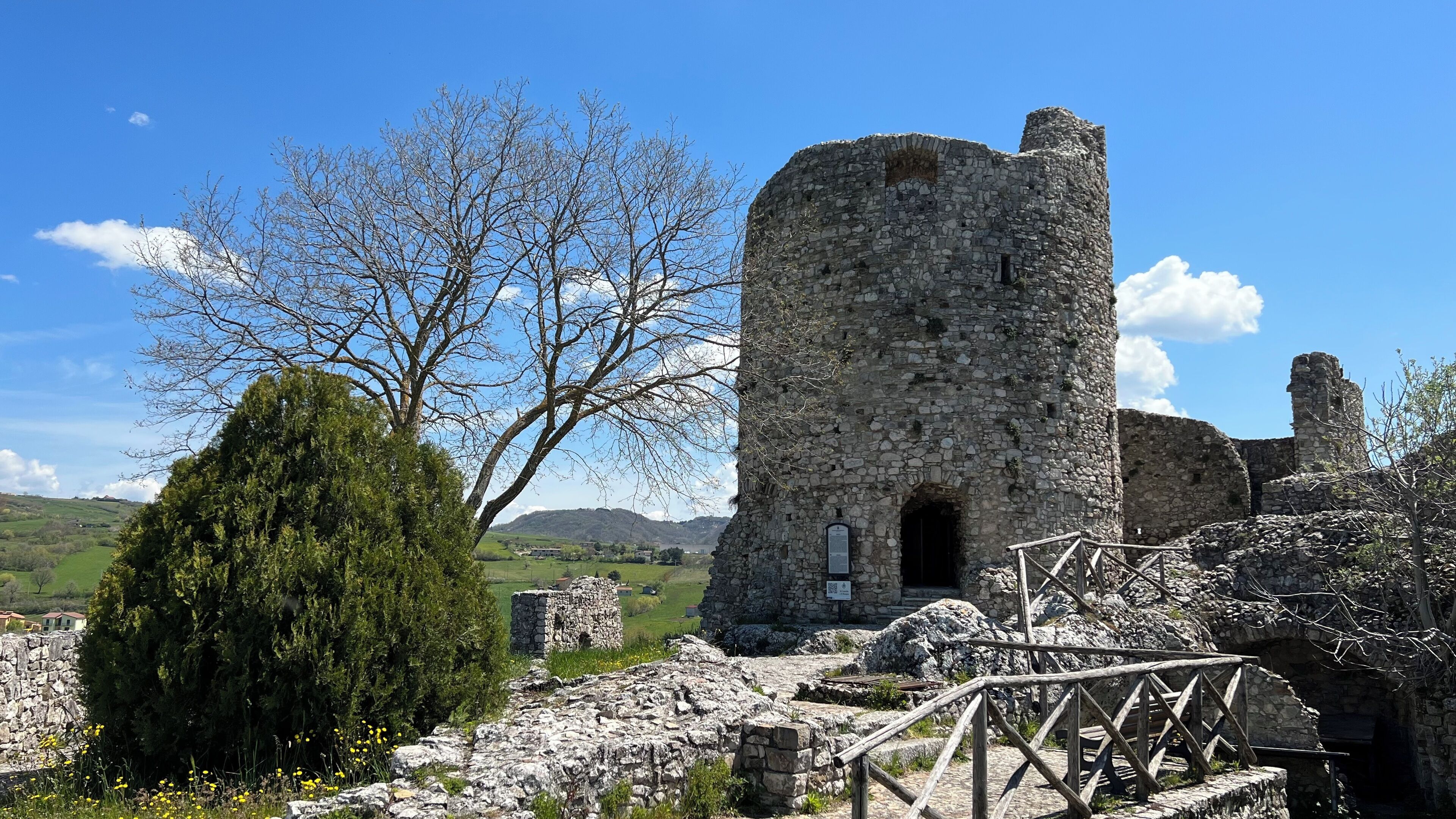 A stone ruin with a tower, surrounded by trees and a clear sky.