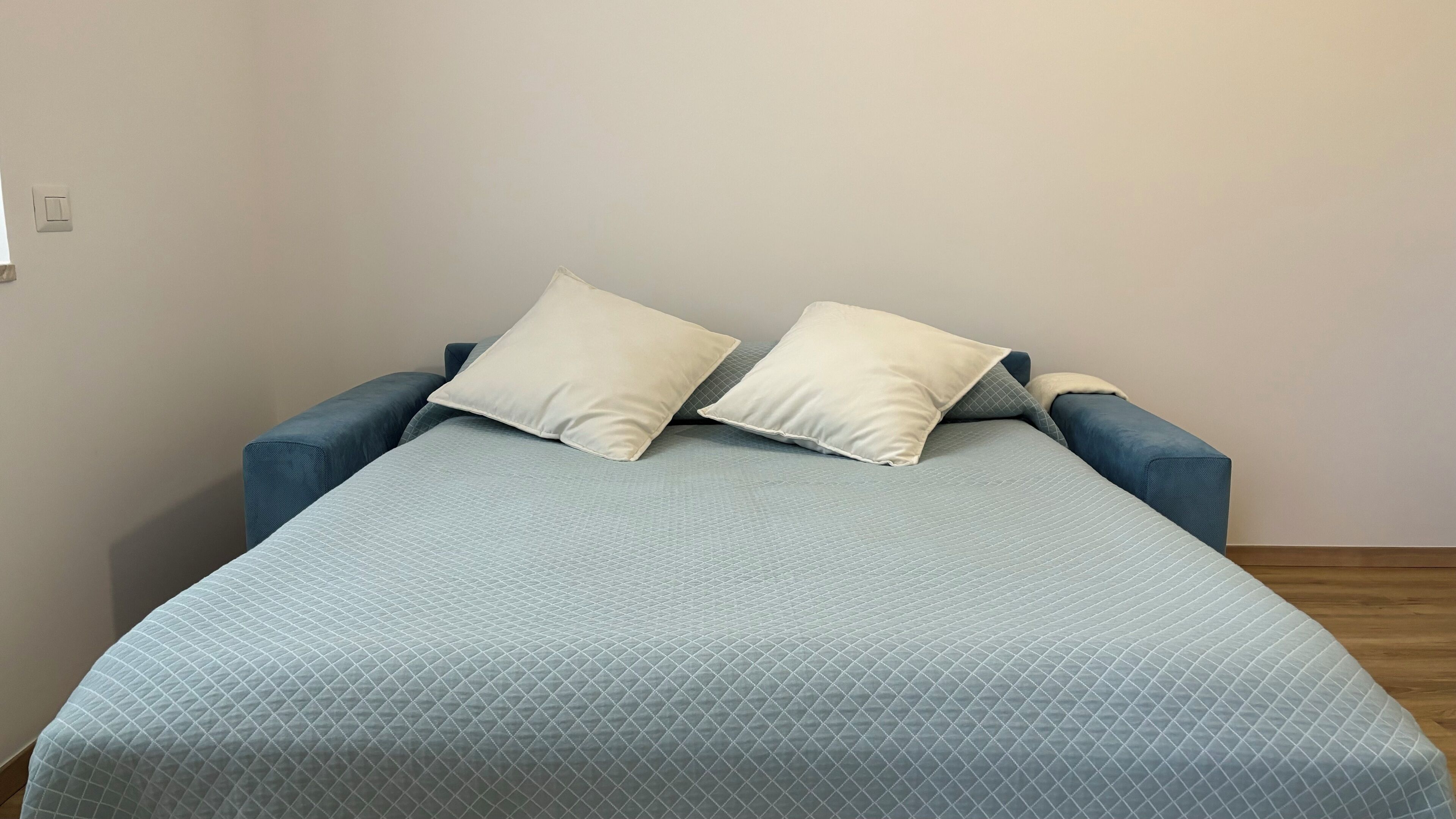 Een bed met een geborduurde blauwe deken en twee witte kussens.