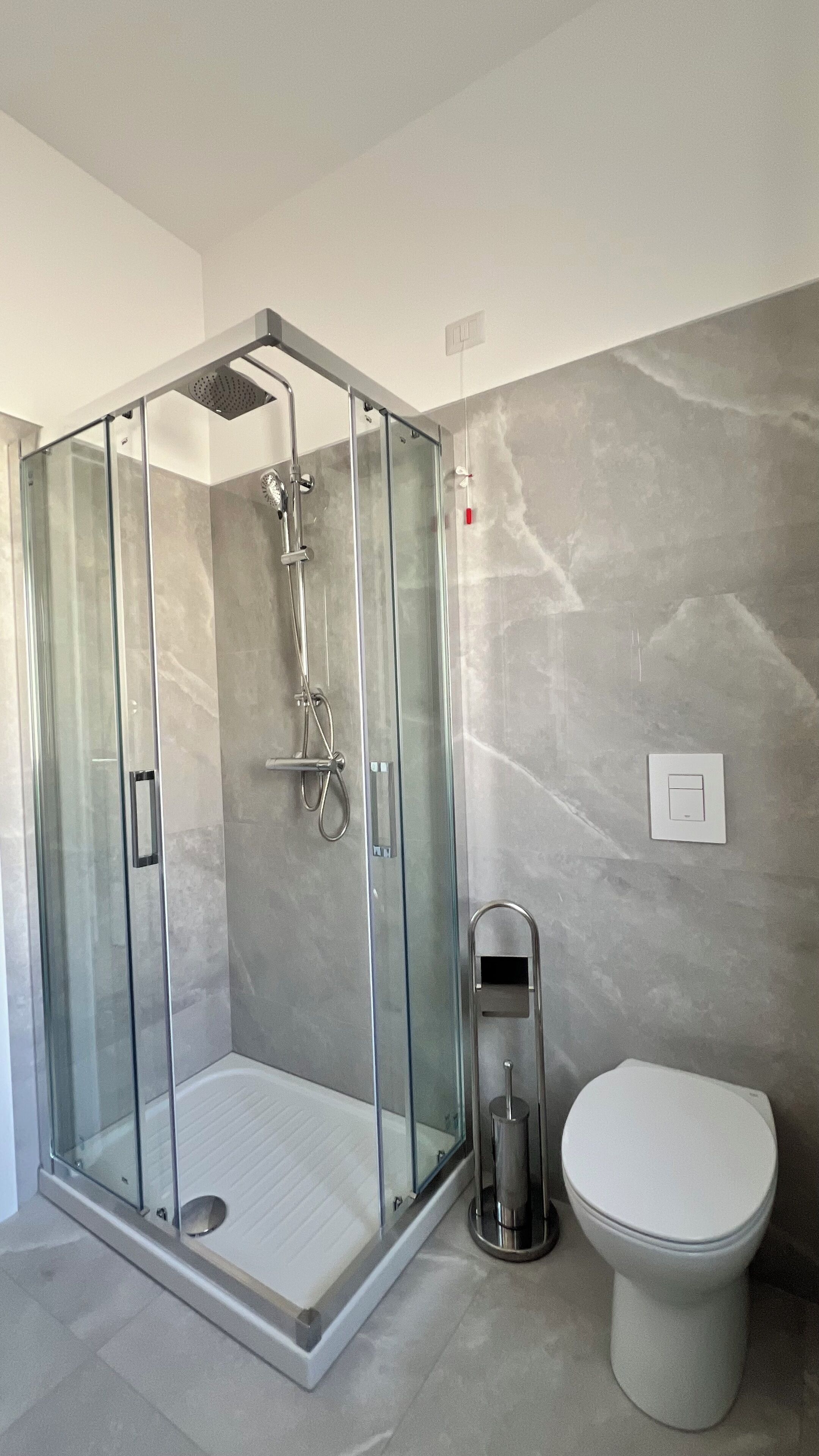 A modern bathroom with a glass-enclosed shower, a toilet, and a marble wall.