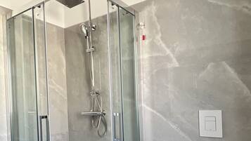 A modern bathroom with a glass-enclosed shower, a toilet, and a marble wall.