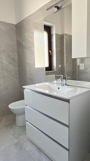 Une salle de bain moderne avec un meuble-lavabo blanc, un grand miroir et des toilettes.