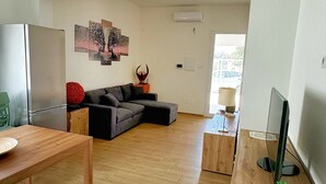 Un amplio salón con suelo de madera, un sofá modular gris, una mesa de comedor y un televisor sobre un mueble de madera.