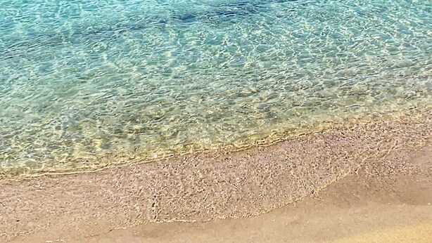 Una playa con agua turquesa cristalina, una orilla de arena y una persona en un bote a lo lejos.