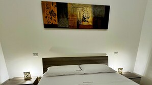 Una cama bien hecha con sábanas blancas y tres toallas dobladas con el texto 'Casa Olivares', un cabecero de madera y una obra de arte en la pared sobre la cama.