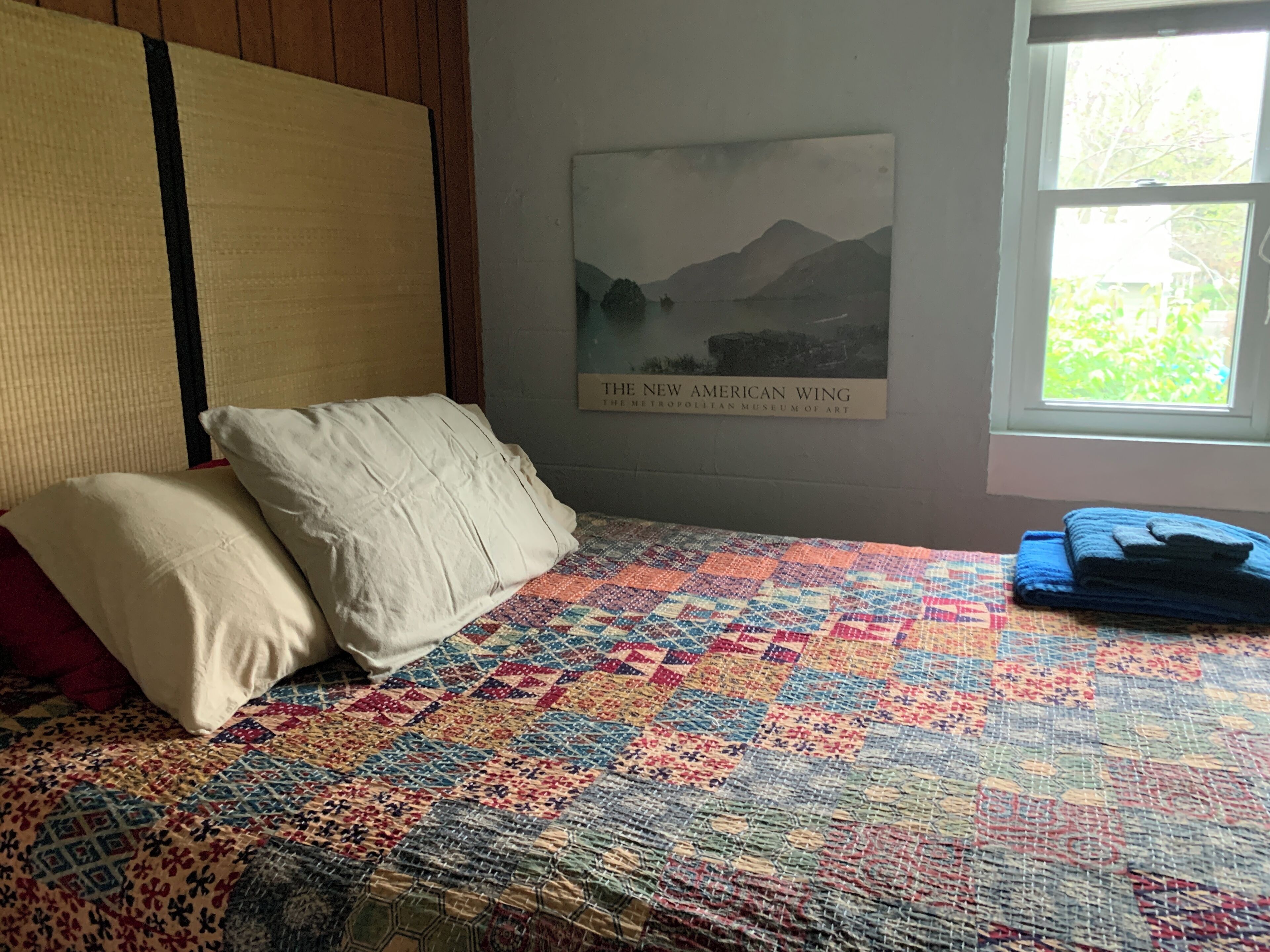 Un lit avec une couverture colorée, des oreillers et une affiche accrochée au mur.