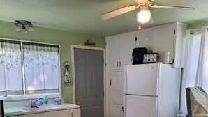 Una cocina compacta con refrigerador, estufa y ventilador de techo.