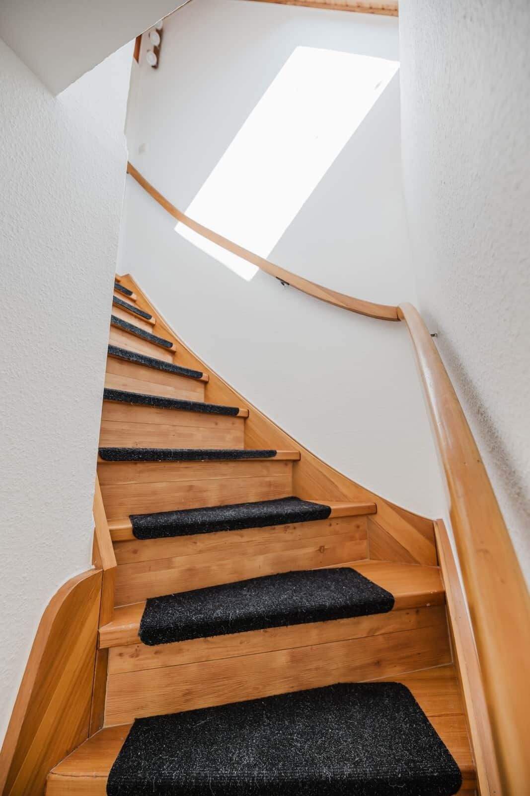 A wooden staircase with black carpeted steps and a skylight above.