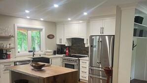 A modern kitchen with white cabinets, a central island with stools, a stainless steel refrigerator, and a stone backsplash. - 5 min walk to the beaches of Georgian Bay
Family fun cottage, 2026- 063 (Ishpiming Beach)
