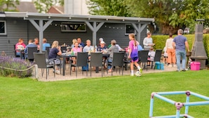 Un espacio de comedor al aire libre con mesas y sillas, una zona de estar cubierta y un césped.