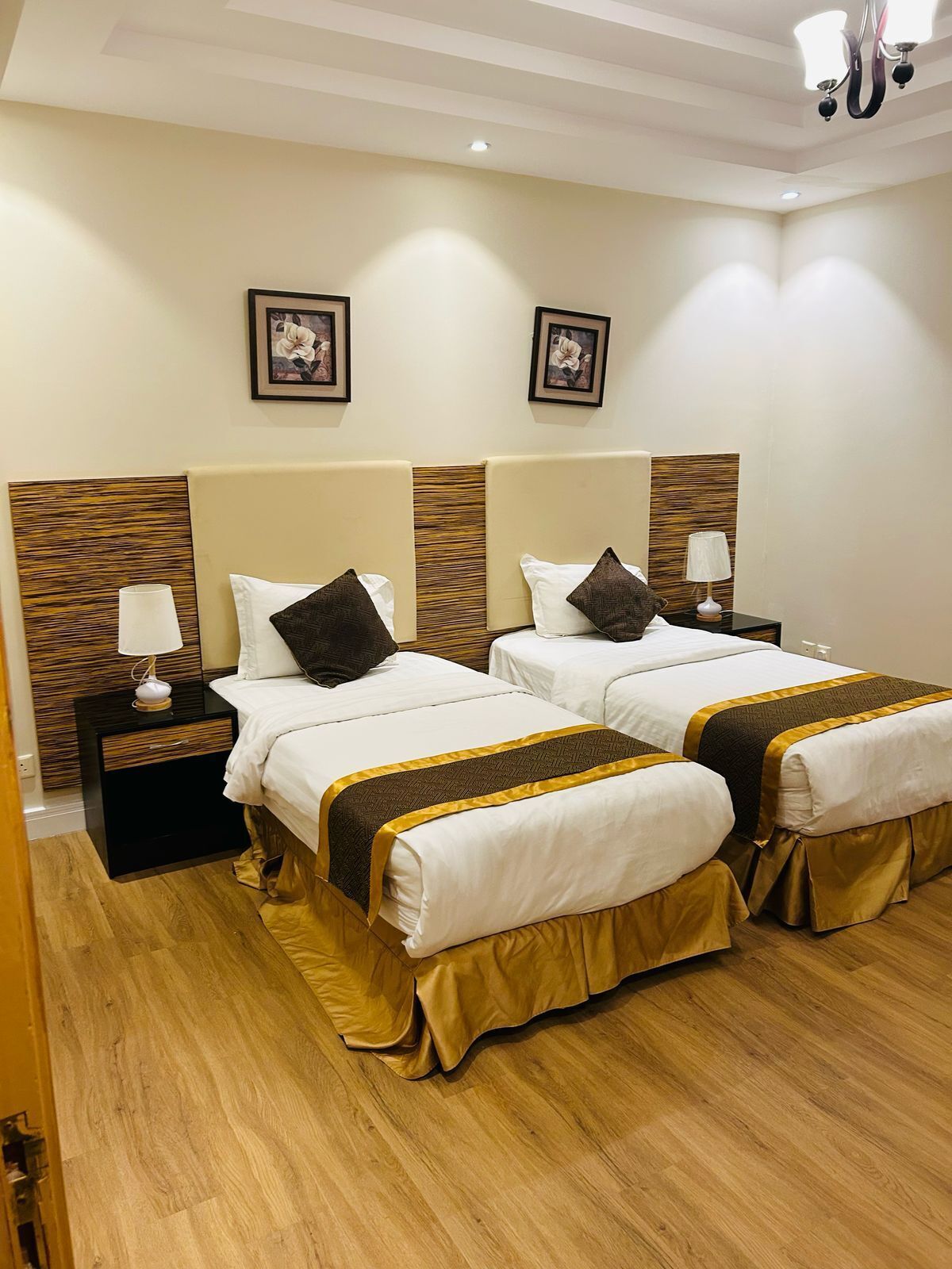 A hotel room with two beds, wooden headboards, bedside tables with lamps, and framed pictures on the wall.