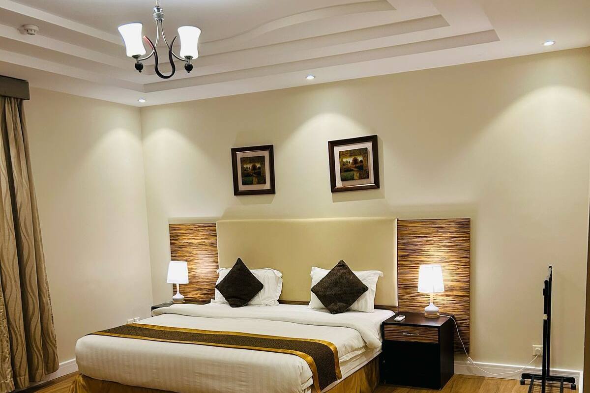 A hotel room with a large bed, two bedside tables with lamps, wooden headboard, and a ceiling fan.