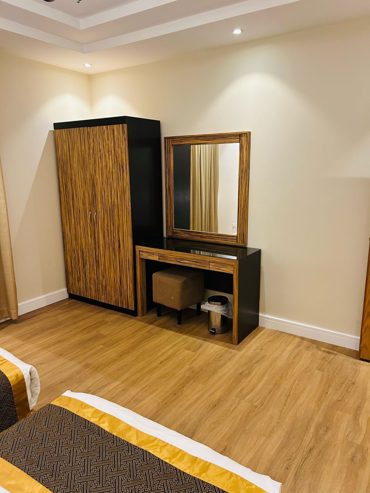 A hotel room with a wooden desk, a mirror, a trash bin, and a bed with a patterned bedspread.