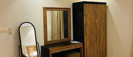 Una habitación con piso de madera, un escritorio negro con espejo, un armario y una silla negra.