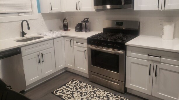 Una cocina moderna con armarios blancos, una estufa de acero inoxidable, un microondas y un lavavajillas.