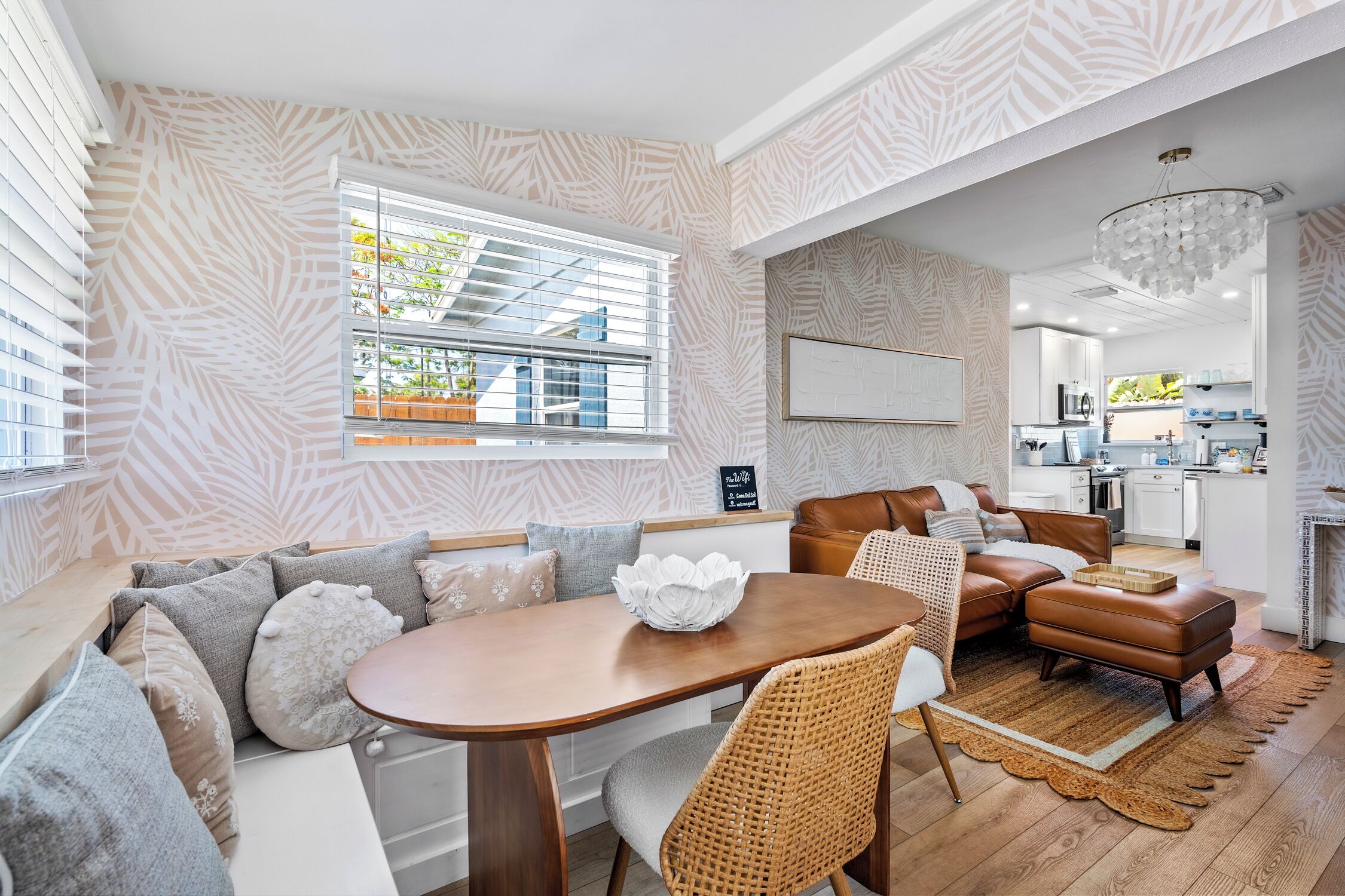A modern living room with a wooden dining table, a brown leather sofa, and a woven chair.