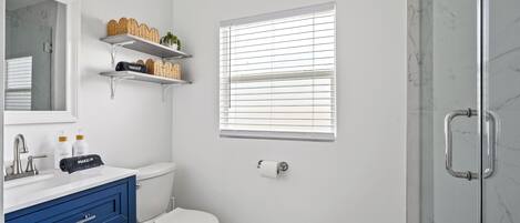 A bathroom with a white toilet, a blue vanity, a mirror, and a window with blinds.