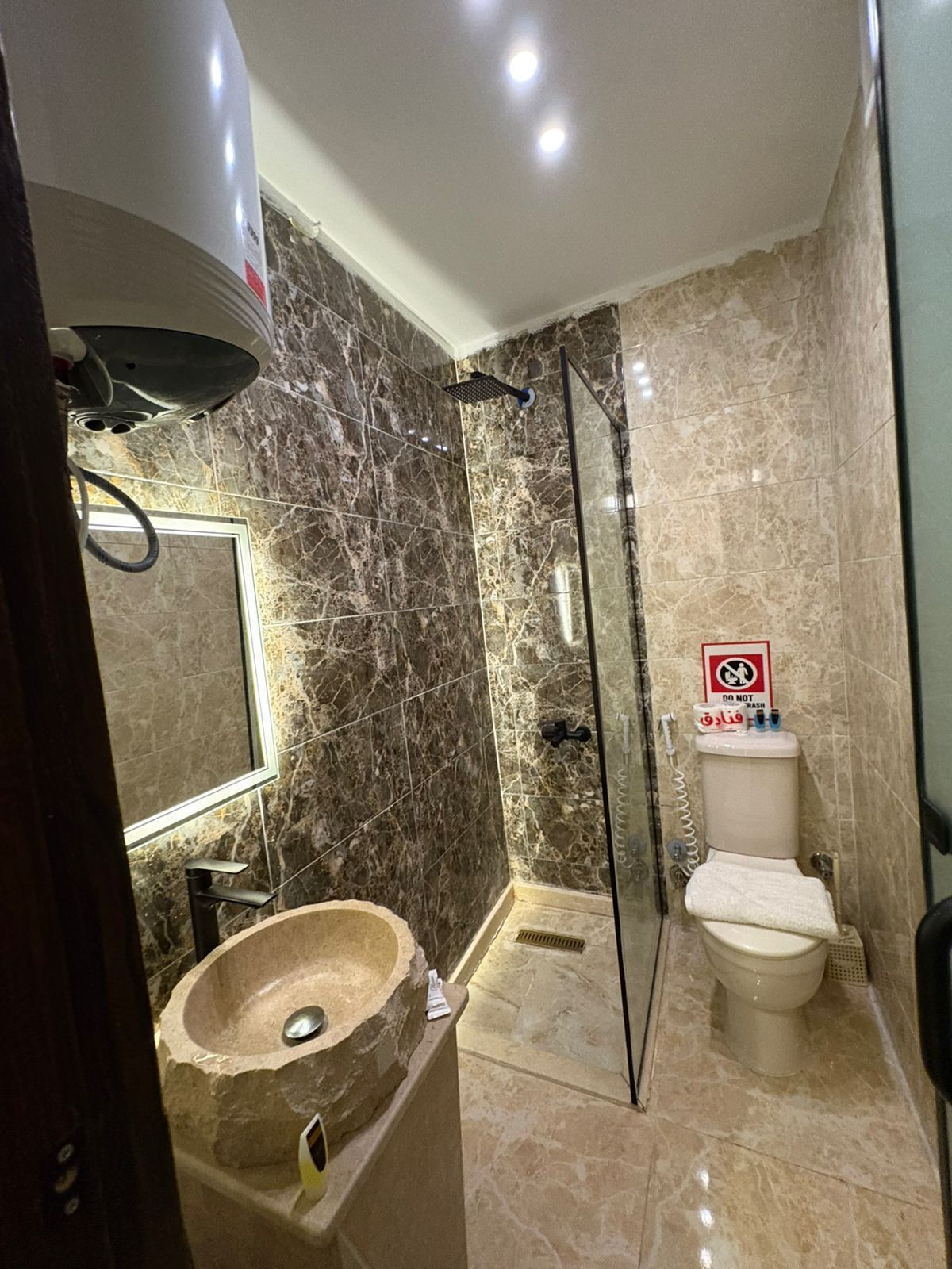 Une salle de bain avec un mur en marbre, une douche en verre, des toilettes et un lavabo avec un receveur en pierre.