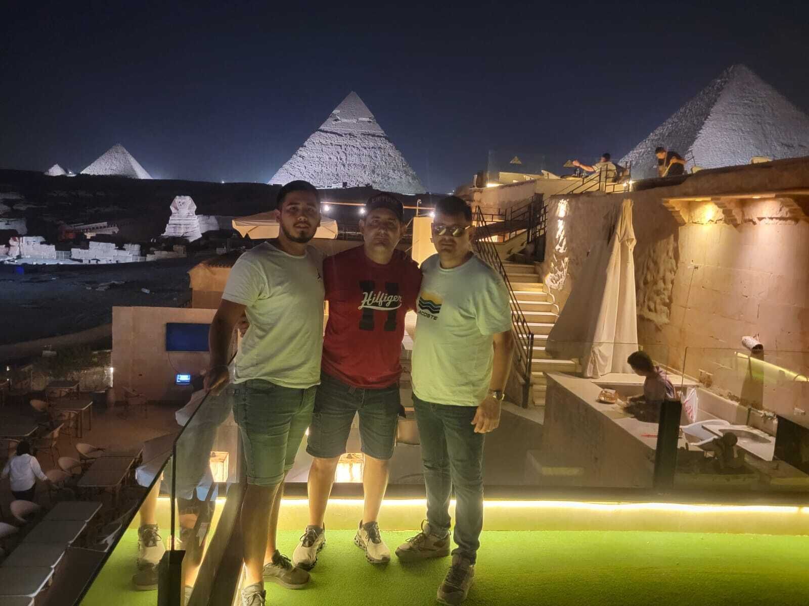 Tres personas de pie en un balcón con vistas a las pirámides al fondo.