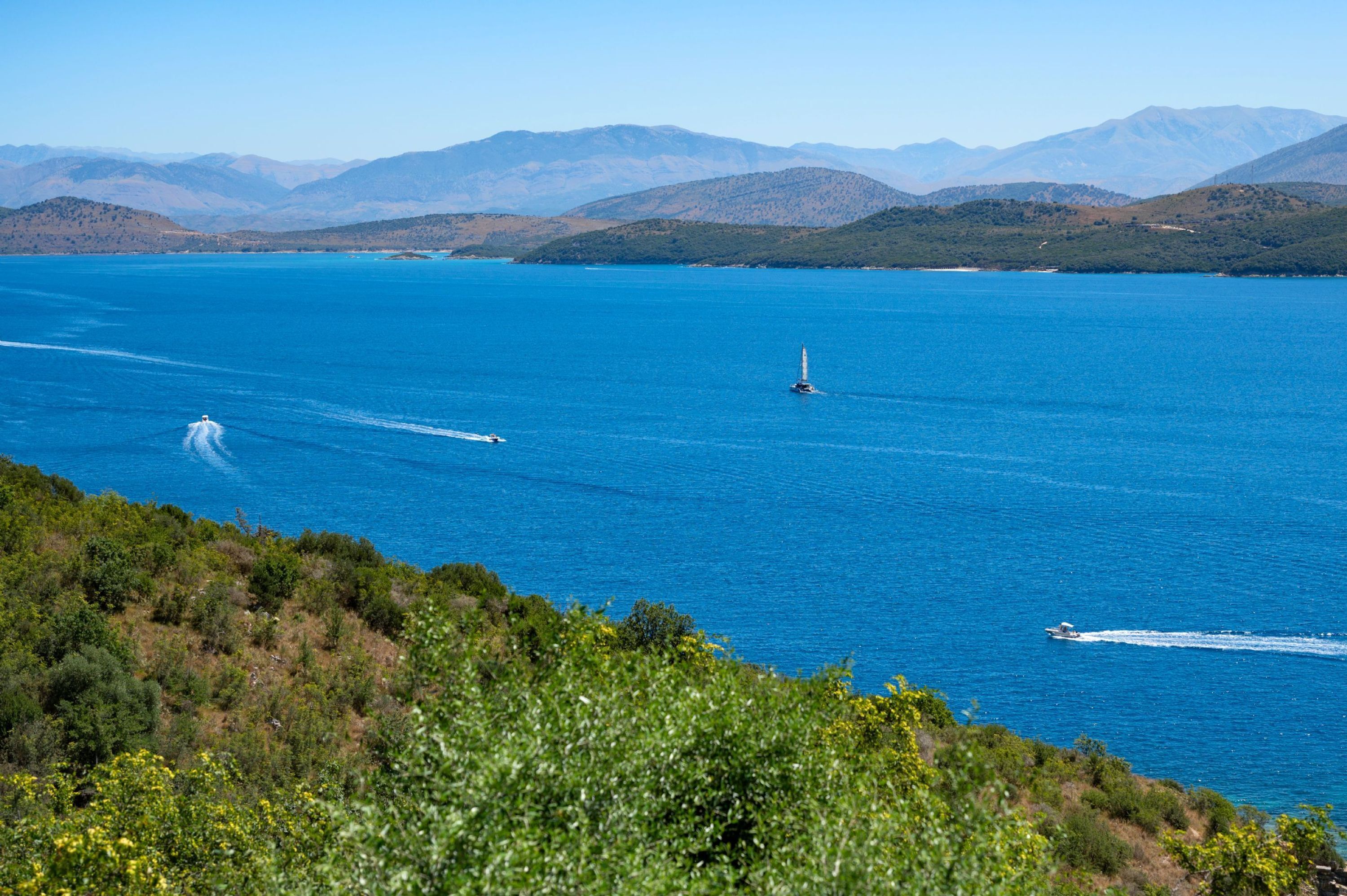 Un paisaje costero con un mar azul cristalino, un faro y montañas a lo lejos.