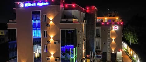 A hotel with a modern design, featuring a prominent neon sign, multiple air conditioning units, and a well-lit entrance.