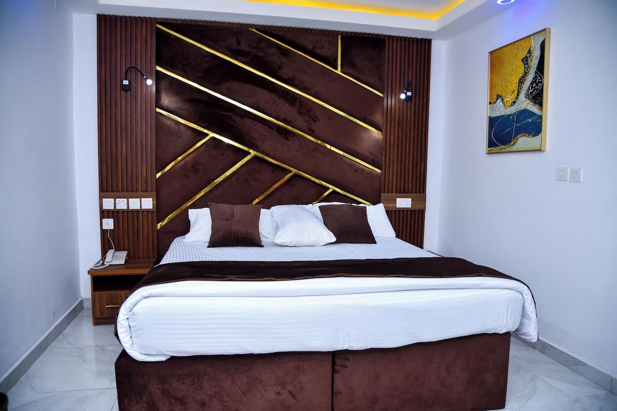 A modern bedroom with a large bed, wooden headboard with gold accents, bedside lamps, and a painting on the wall.