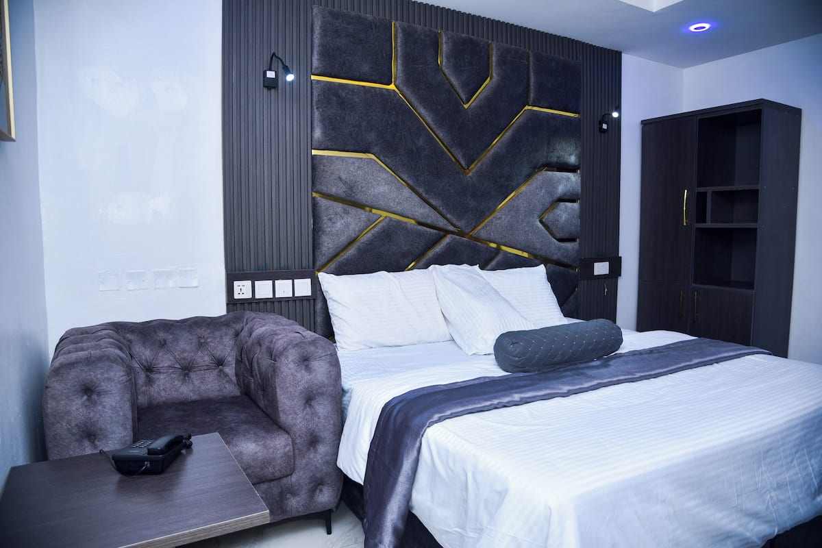 A modern bedroom with a tufted sofa, a bed with white linens, and a decorative headboard with geometric patterns.