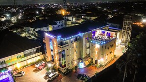 Un edificio a più piani con un bar sul tetto e zona salotto all'aperto, circondato da auto parcheggiate e un parcheggio.