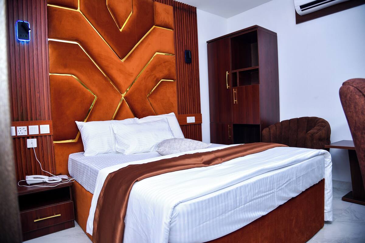 A hotel room with a large bed, wooden headboard, and a wardrobe.