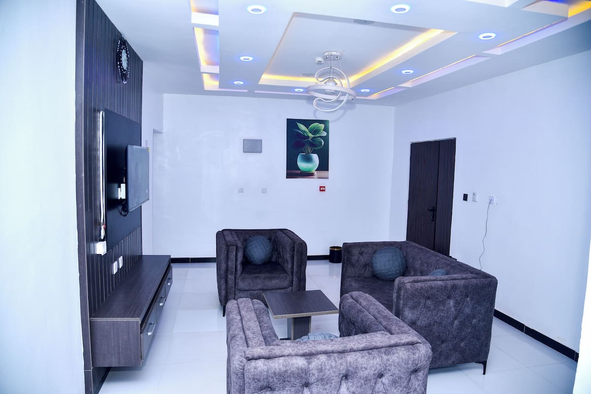 A modern living room with a flat-screen TV, two armchairs, a sofa, and a small table.