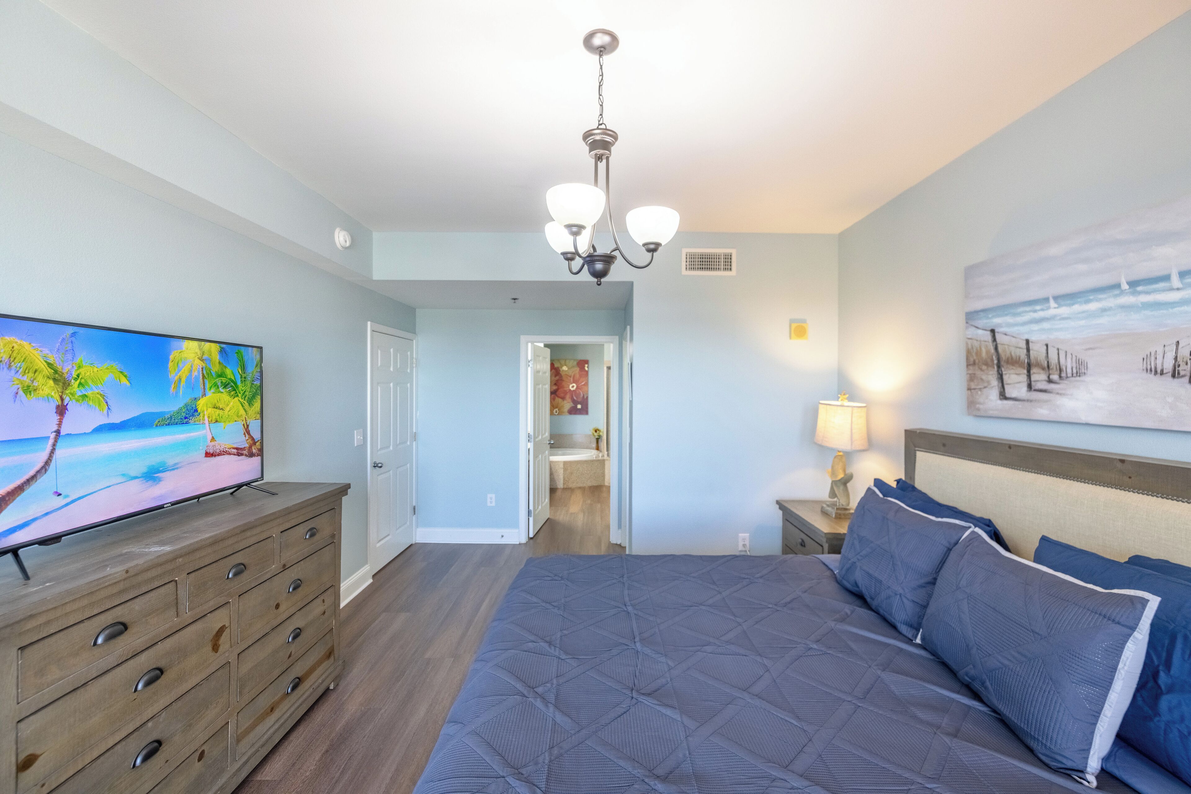 Un dormitorio con una cama grande, un televisor en una cómoda, un cuadro en la pared y un pasillo que conduce a otra habitación.